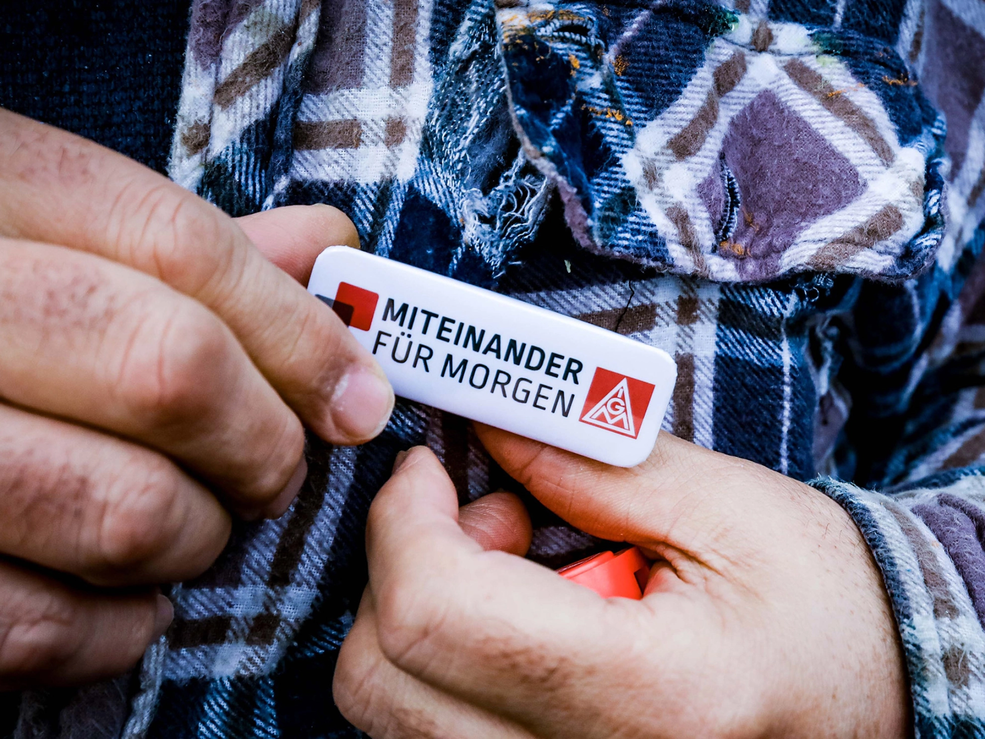 ann steckt IG-Metall-Pin an sein kariertes Hemd.